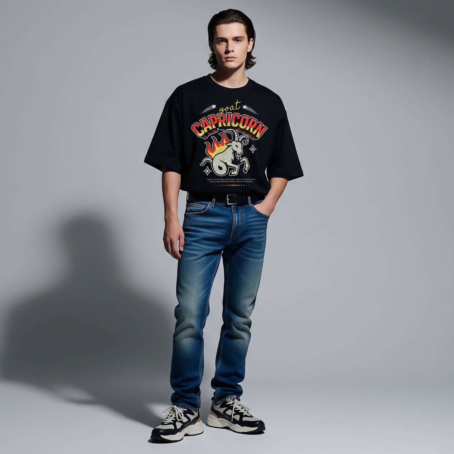 Person wearing a black t-shirt with a graphic design and blue jeans on a gray background