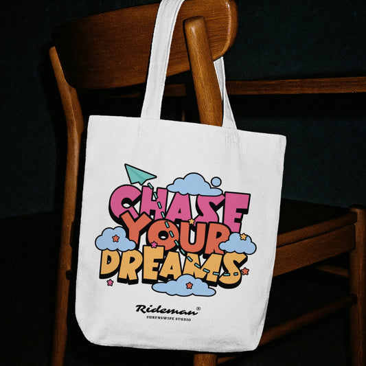 White tote bag with colorful text 'Chase Your Dreams' on a wooden chair.