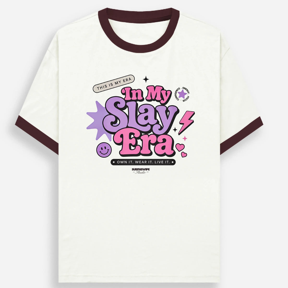 An off-white ringer t-shirt with dark brown ribbed collar and sleeve cuffs, featuring a colorful graphic on the chest that reads 'In My Slay Era' in purple and pink bubble letters with star and lightning accents.