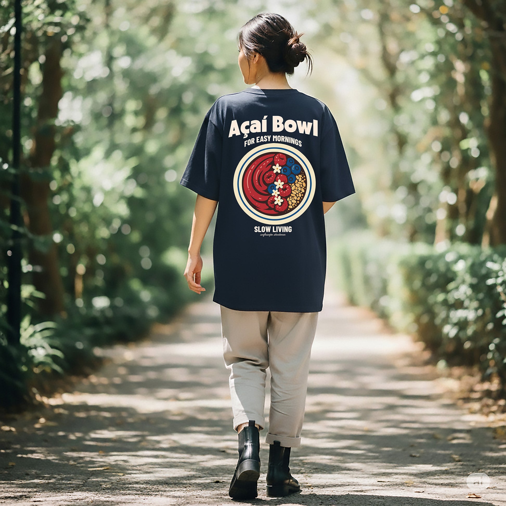Person wearing a navy blue t-shirt with a colorful graphic and text, walking through a forest.