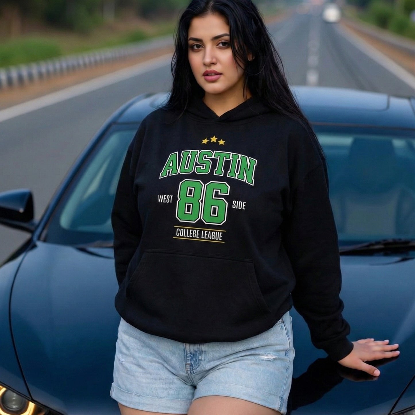 Woman wearing a black hoodie with 'Austin 86' text, standing next to a blue car on a road.