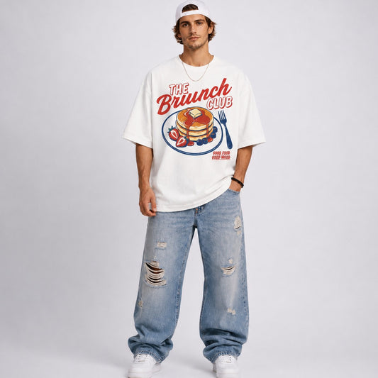 Person wearing a white t-shirt with 'The Brunch Club' design and ripped jeans on a plain background