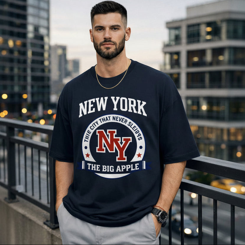 Man wearing a navy blue t-shirt with 'New York' text and design, standing on a balcony with cityscape background.