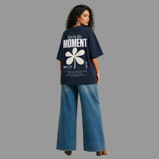 Woman wearing a navy blue t-shirt with a white flower design and text on the back, standing against a gray background.