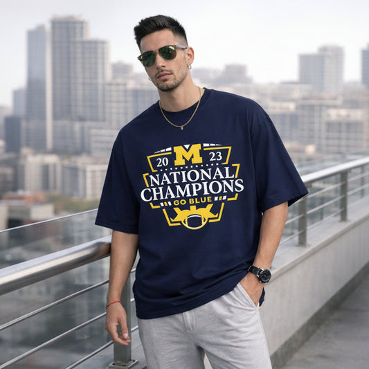Man wearing a navy blue t-shirt with '2023 National Champions' text and graphics, standing on a rooftop with cityscape background.