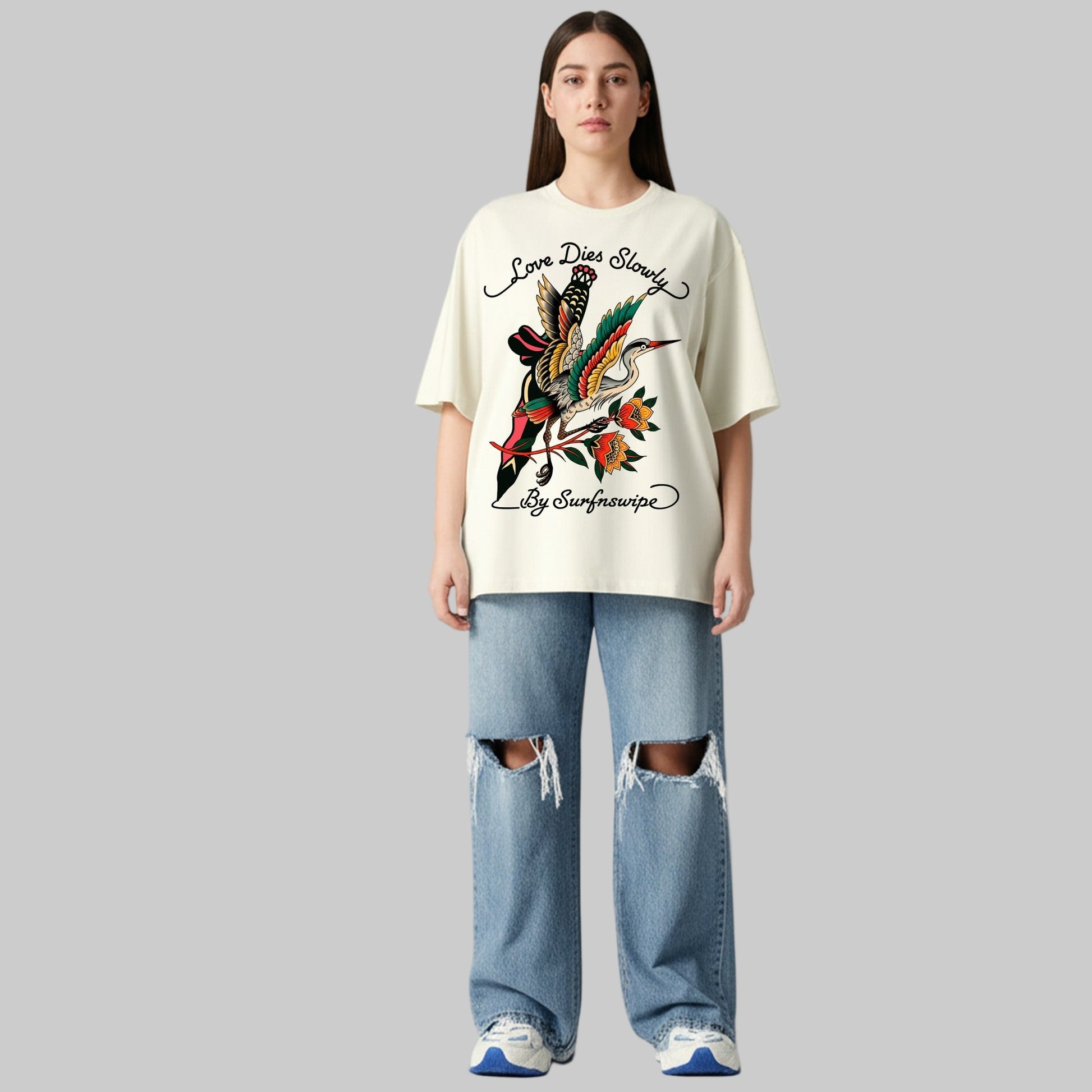 Person wearing a white t-shirt with a graphic design and ripped jeans on a plain background