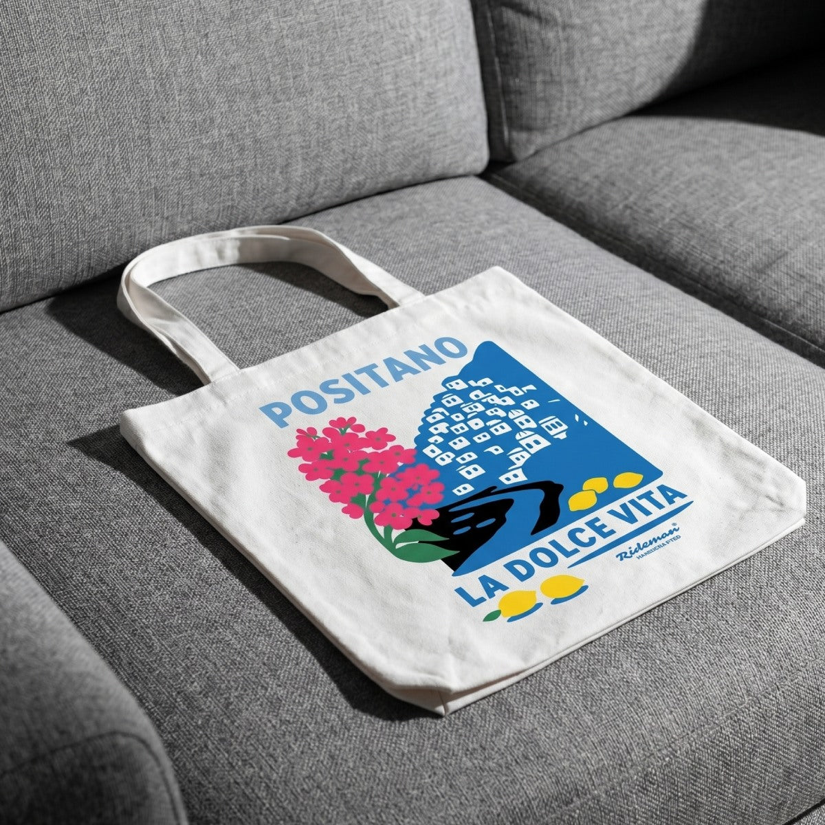 Tote bag with 'Positano La Dolce Vita' design on a gray couch