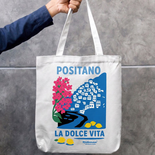 Tote bag with 'POSITANO LA DOLCE VITA' design held by a person against a gray background