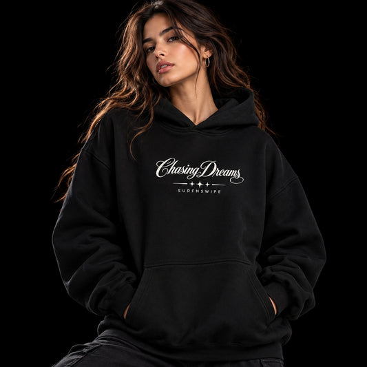 Woman wearing a black Chasing Dreams oversized hoodie with white chest lettering, star details and a kangaroo pocket.