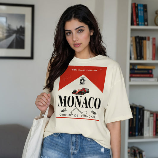 Woman wearing a white t-shirt with Monaco branding in a room with books and a picture.
