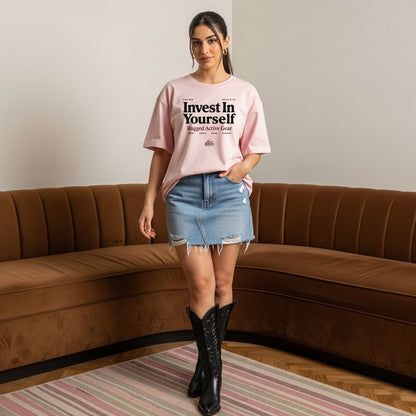 Woman wearing a pink t-shirt with text, denim skirt, and black boots in a living room.