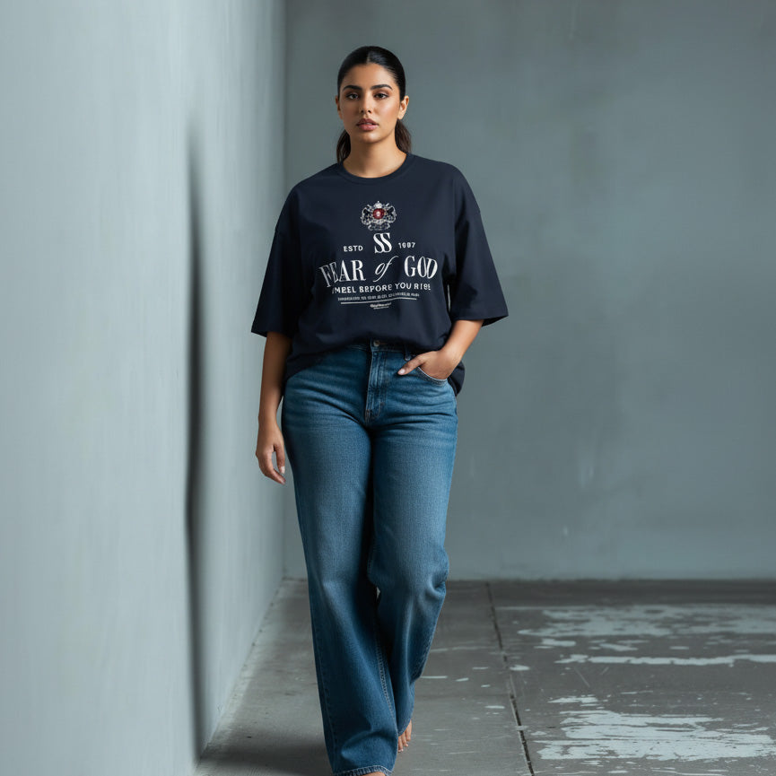 Woman wearing a black t-shirt and blue jeans against a gray wall.