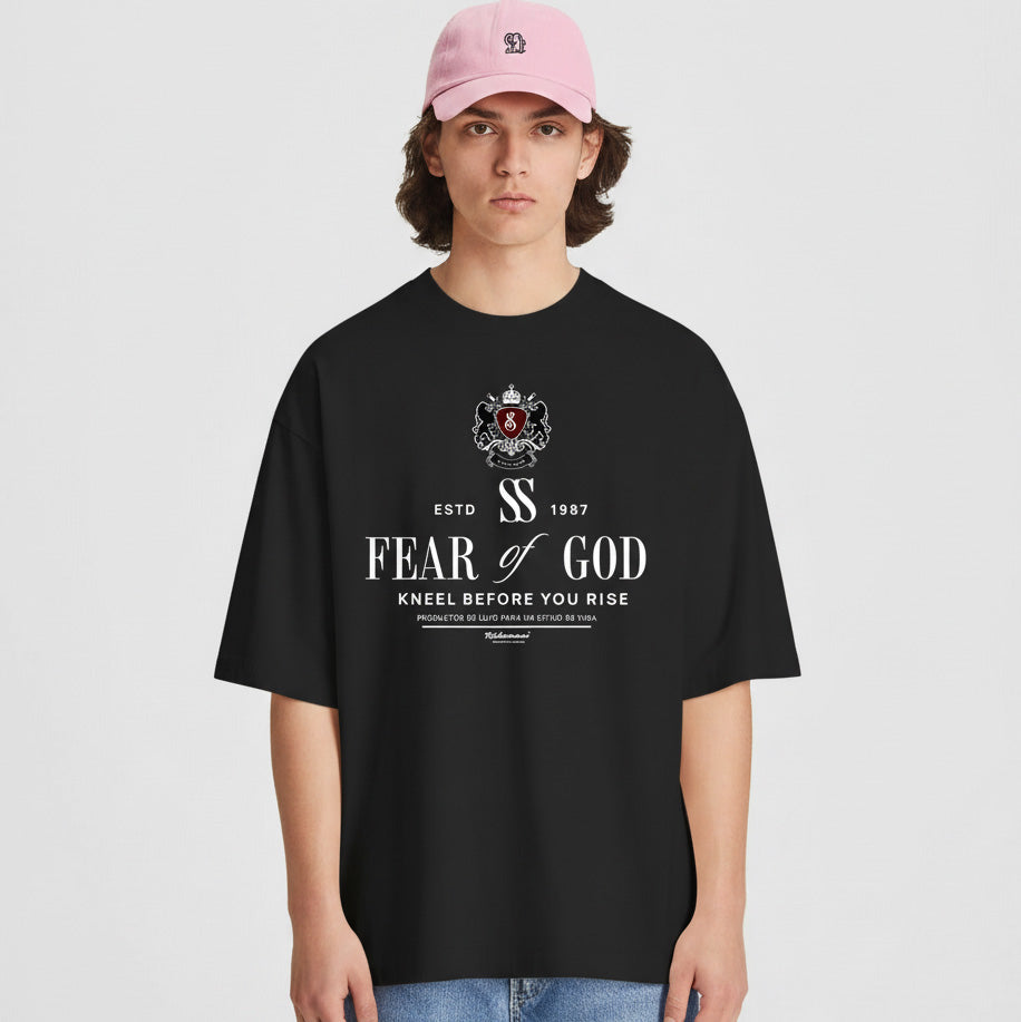 Person wearing a black 'Fear of God' t-shirt with a pink cap on a light gray background