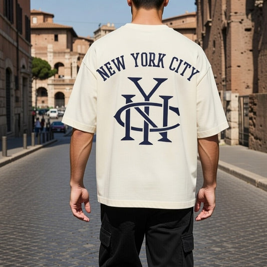 Person wearing a 'New York City' t-shirt with a logo, walking on a street with historical architecture.