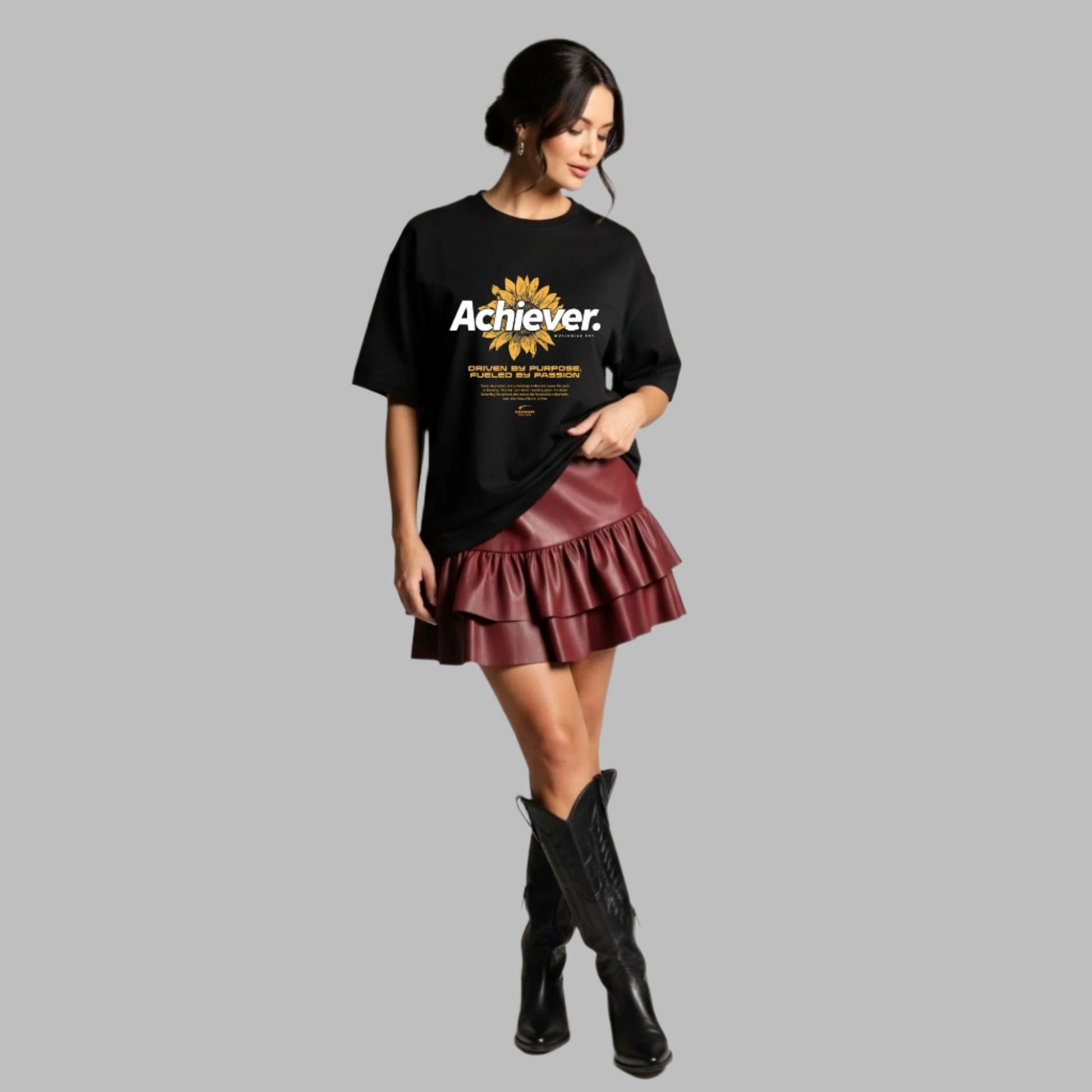 Woman wearing a black t-shirt with 'Achiever' text, burgundy ruffled skirt, and black boots on a neutral background