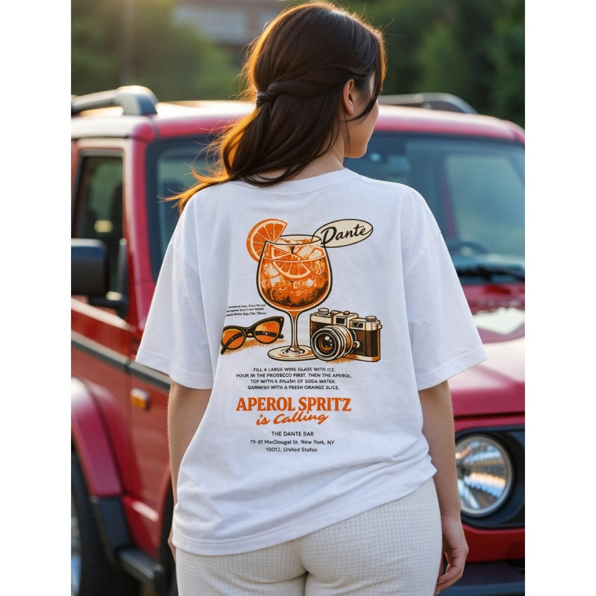 Person wearing a white t-shirt with a graphic design in front of a red vehicle.