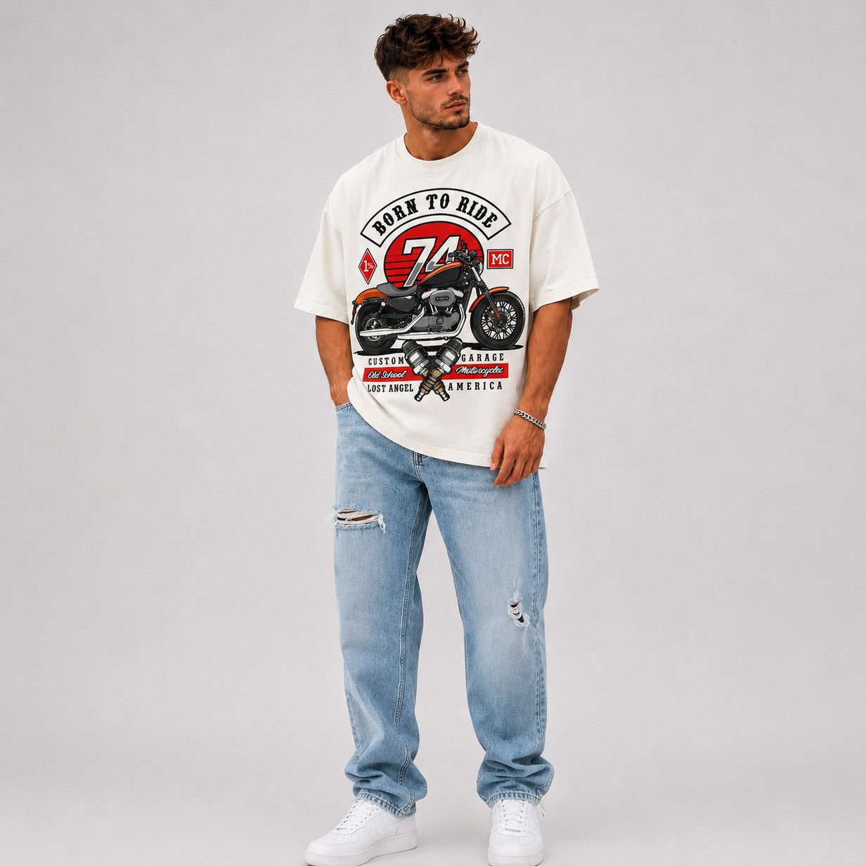 Man wearing a white vintage motorcycle  t-shirt with a motorcycle graphic and text, paired with light blue jeans on a gray background.