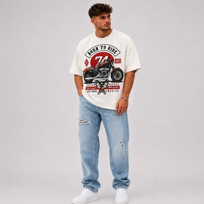 Man wearing a white vintage motorcycle  t-shirt with a motorcycle graphic and text, paired with light blue jeans on a gray background.