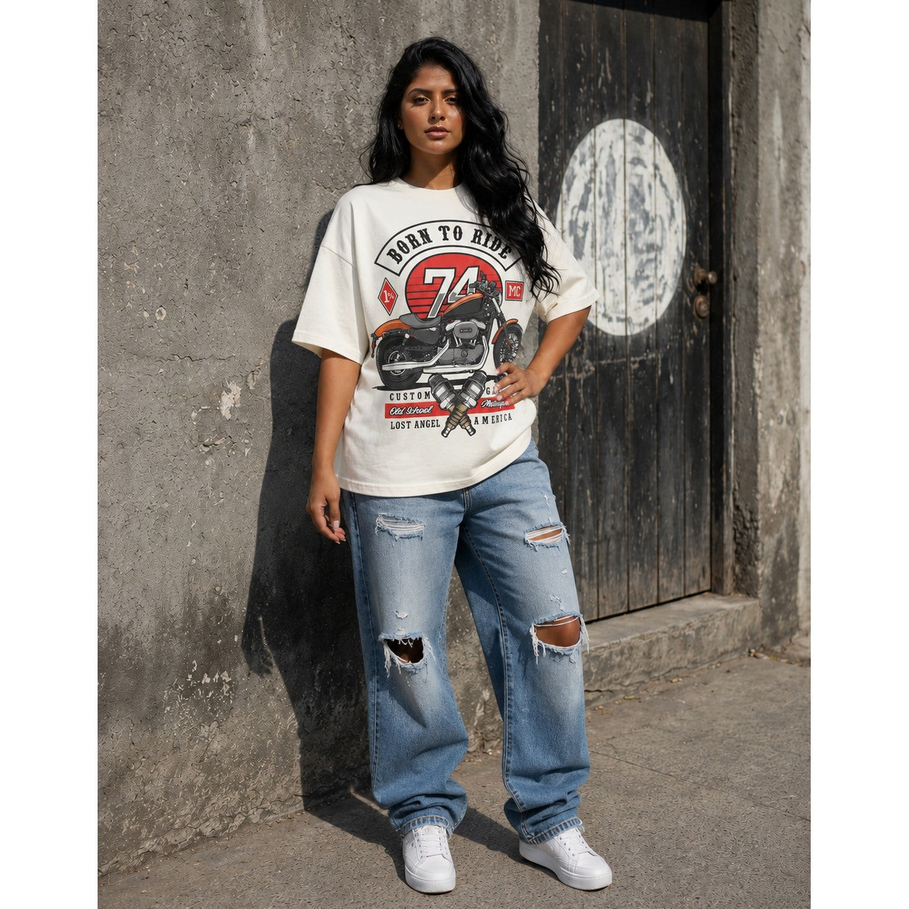 Woman wearing a white vintage motorbike graphic t-shirt and jeans standing against a textured wall.
