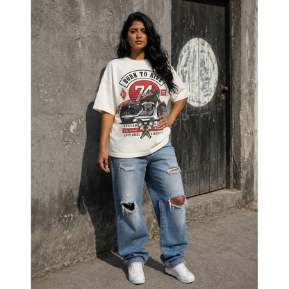 Woman wearing a white vintage motorbike graphic t-shirt and jeans standing against a textured wall.