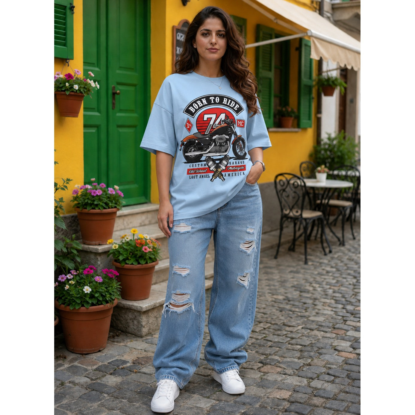 Woman wearing a graphic t-shirt and jeans standing on a street with a yellow building and green door in the background.