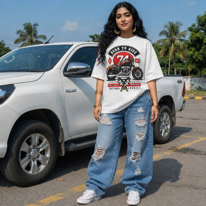 Woman wearing a vintage motorbike graphic t-shirt and ripped jeans standing next to a white truck with palm trees in the background.