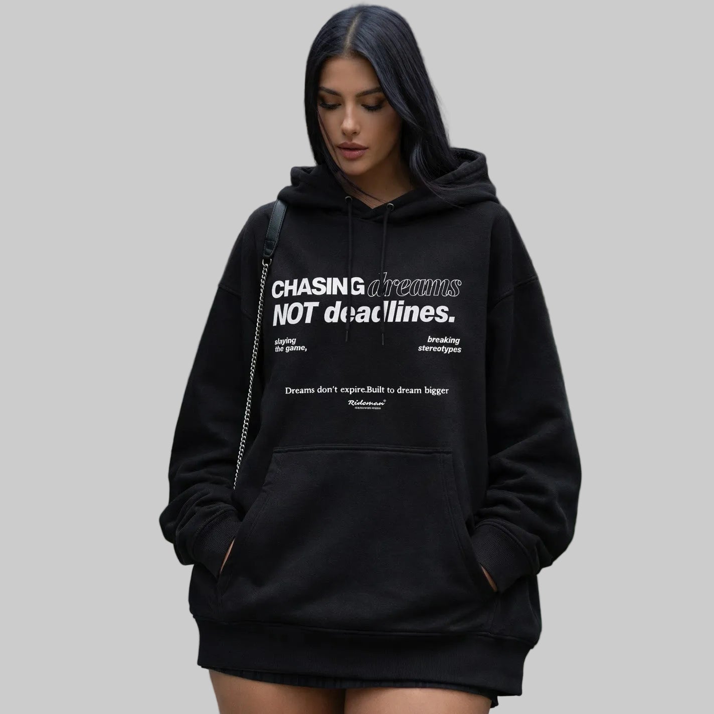 Person wearing a black hoodie with text, standing outdoors with greenery in the background