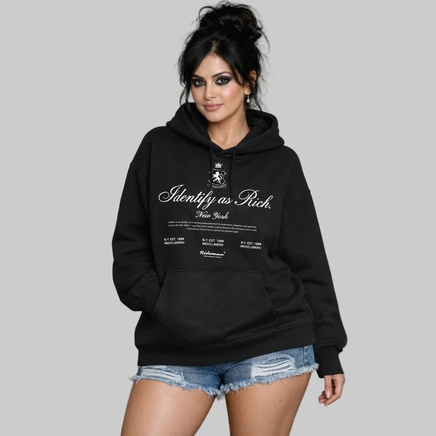 Woman wearing a black hoodie with text and a logo, standing against a neutral background