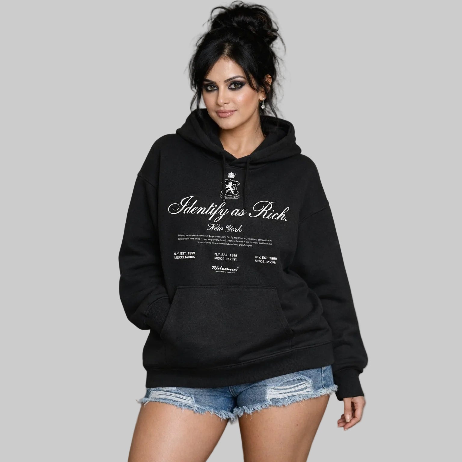 Woman wearing a black hoodie with text and a logo, standing against a neutral background