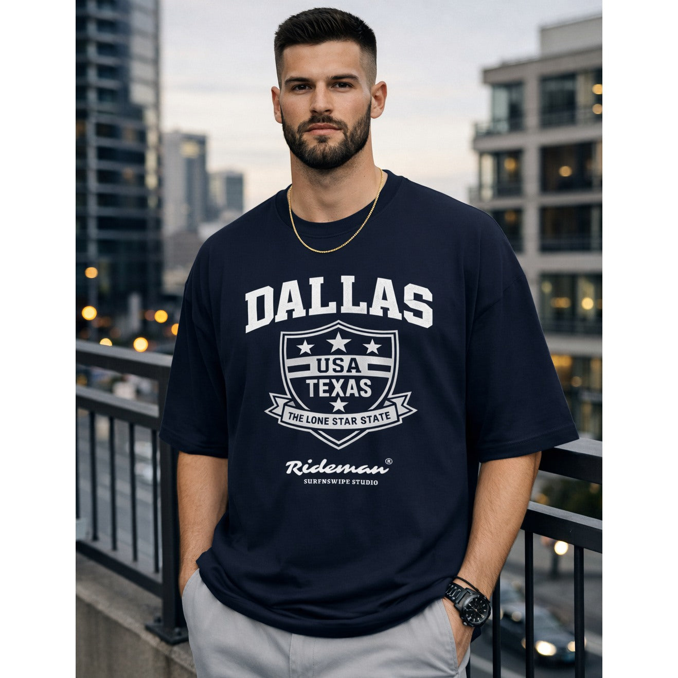 Man wearing a navy blue t-shirt with 'Dallas, USA, Texas' text and graphics, standing on a balcony with cityscape background.
