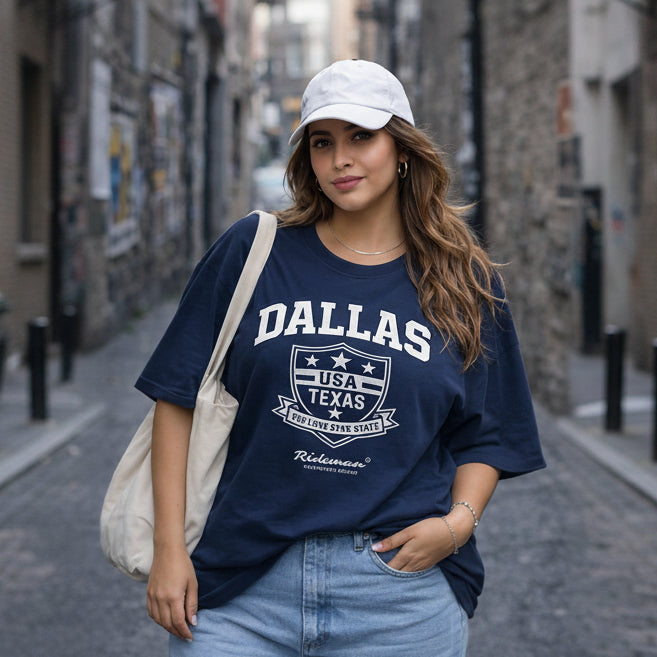Woman wearing a navy blue t-shirt with 'Dallas, USA, Texas' text and graphics, standing on a street.