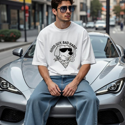 Man sitting on a car wearing a white t-shirt with a graphic design and sunglasses, in an urban setting.