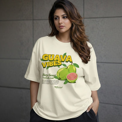 Woman wearing a 'Guava Vibes' t-shirt with guava graphics against a gray tiled wall.