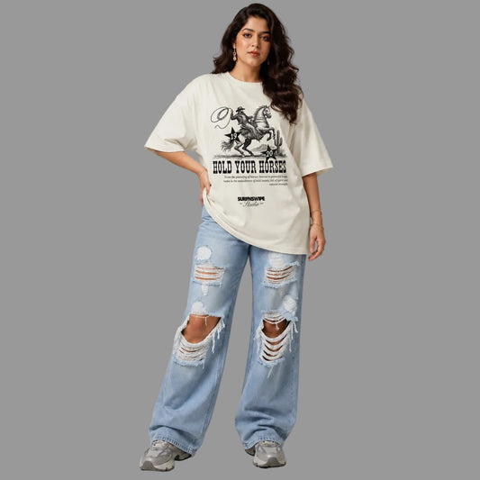 Woman wearing a white oversized t-shirt with graphic design and ripped jeans on a gray background