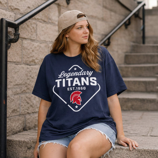 Woman wearing a navy blue t-shirt with 'Legendary Titans' design, sitting against a stone wall.