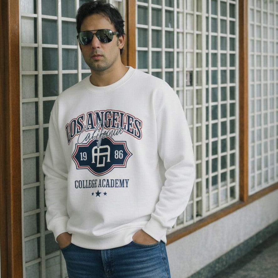 Man wearing a white sweatshirt with 'Los Angeles College Academy' print, standing against a grid-patterned wall.