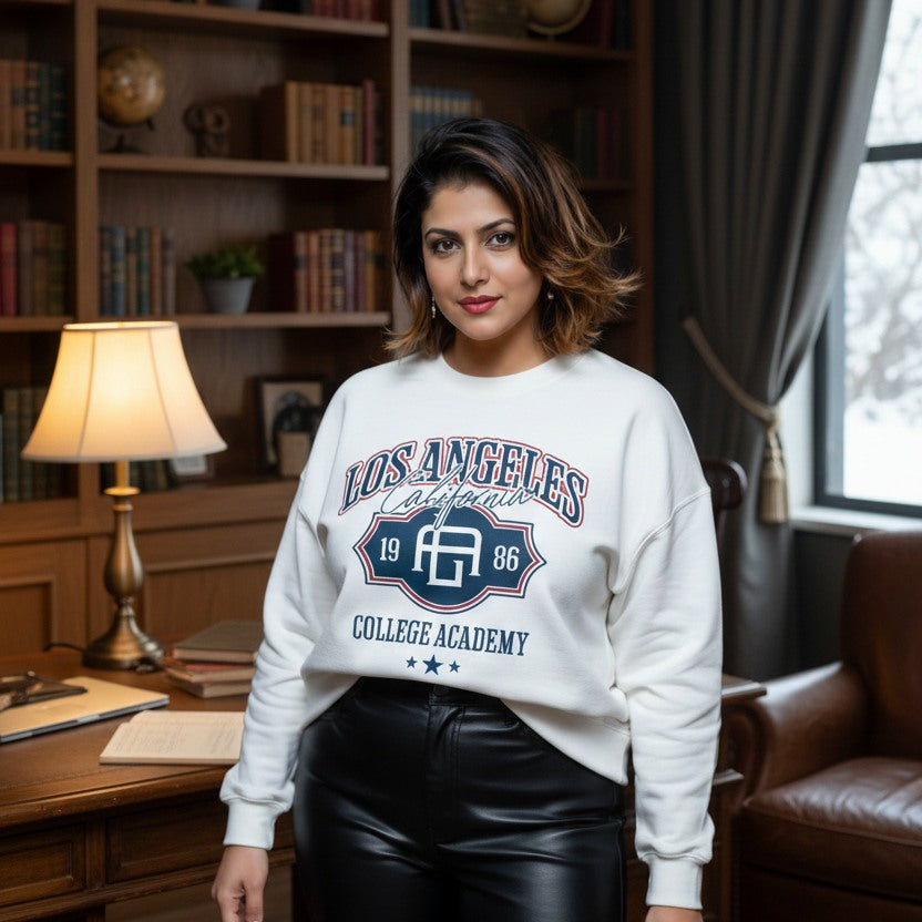 Woman wearing a white sweatshirt with text and graphics in a room with bookshelves and a lamp.