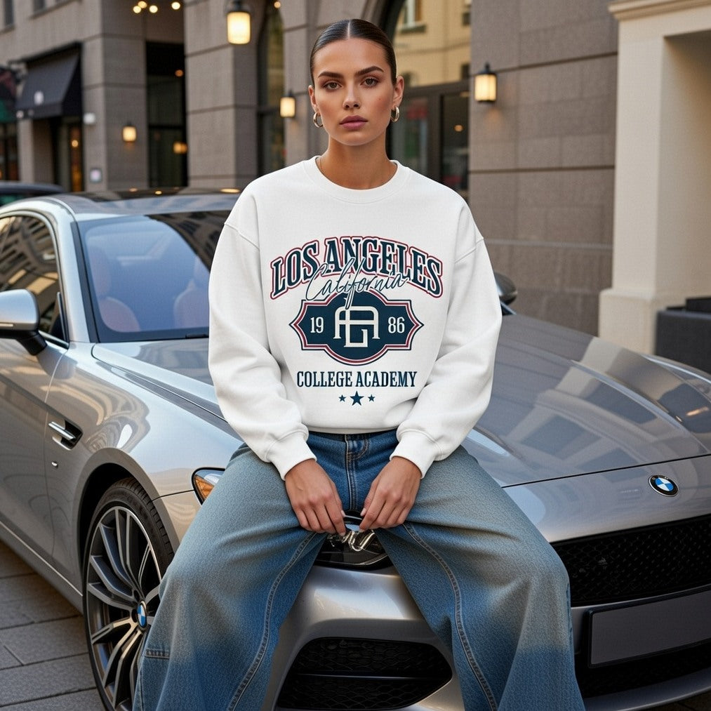 Person wearing a 'Los Angeles College Academy' sweatshirt sitting on a car in an urban setting