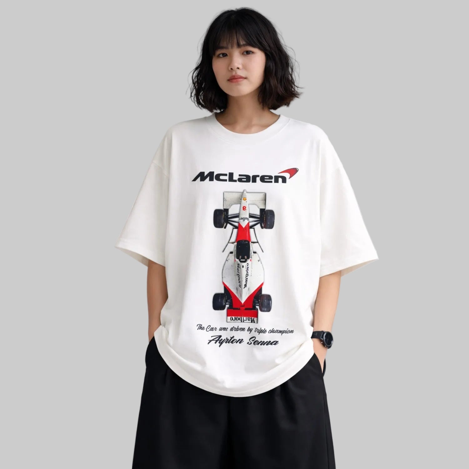 Person wearing a white t-shirt with a McLaren Formula 1 car design on a plain background