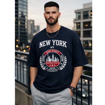 Man wearing a navy blue t-shirt with 'New York' design, standing on a balcony with cityscape background.