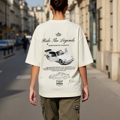 Person wearing a white t-shirt with car graphics and text on a city street.
