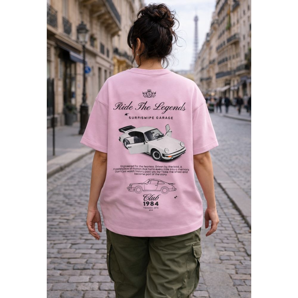 Person wearing a pink t-shirt with car graphics and text on a city street.
