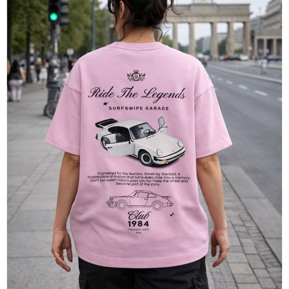 Person wearing a pink t-shirt with car graphics and text in an urban setting
