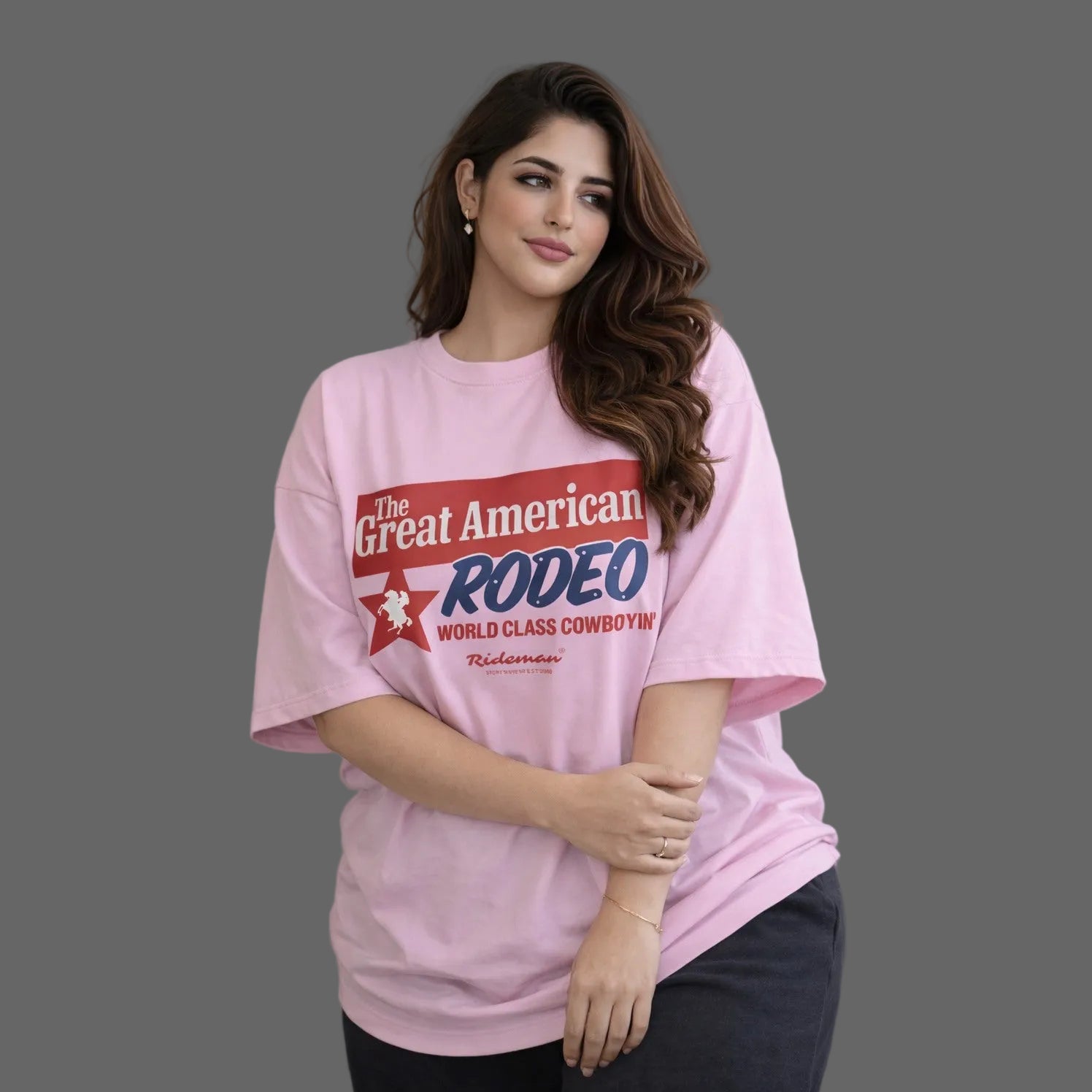 Woman wearing a pink t-shirt with 'The Great American Rodeo' text against a gray wall.
