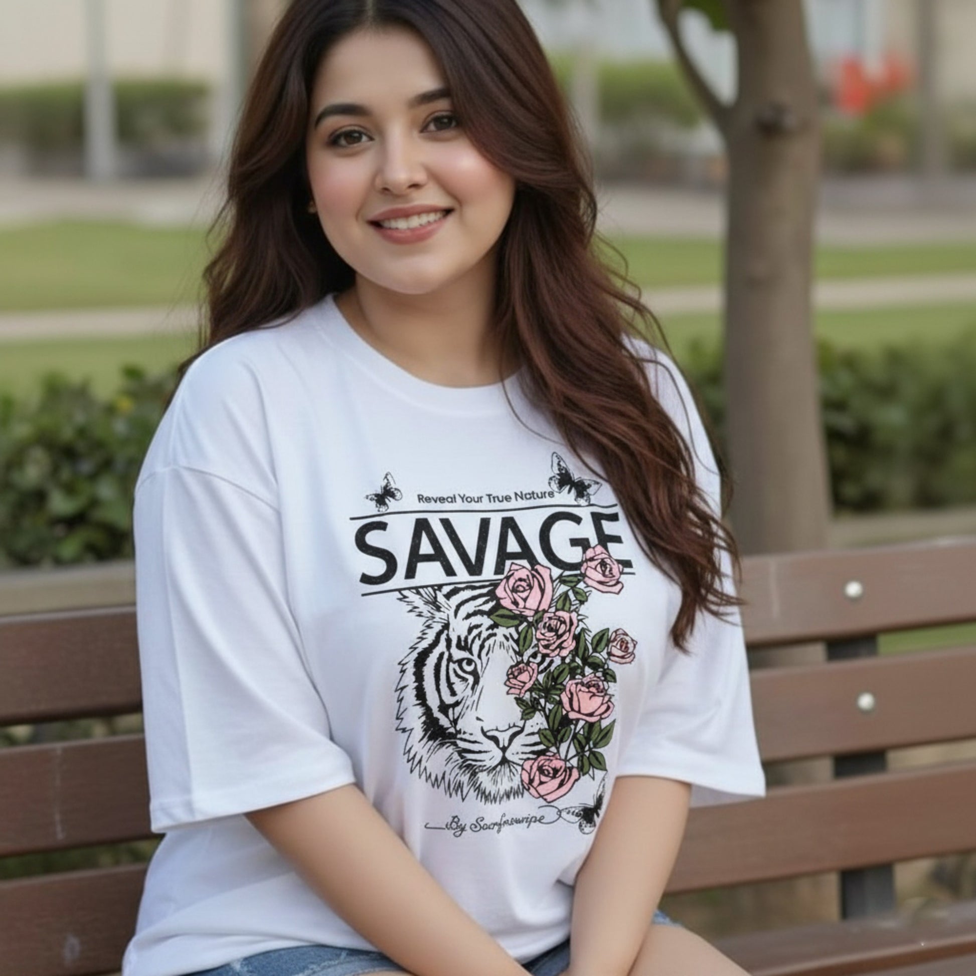 Woman wearing a white t-shirt with a graphic design of a tiger and roses, sitting on a bench outdoors.