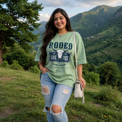Woman wearing a Jade blue t-shirt with 'Rodeo Live Free' design in a living room.