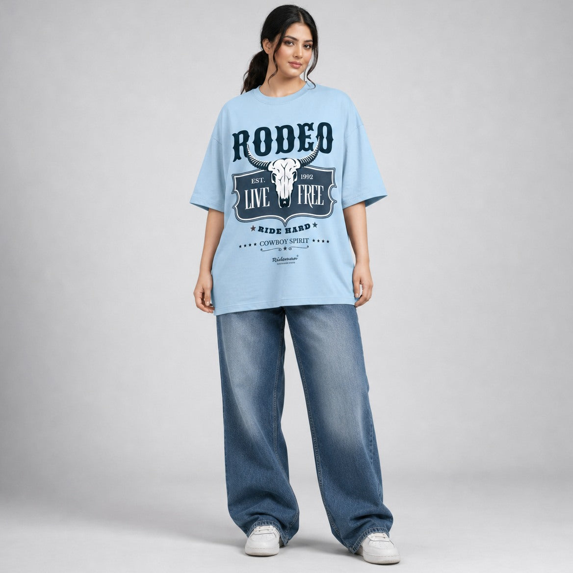Woman wearing a light blue 'Rodeo' t-shirt and jeans on a gray background
