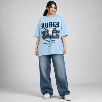 Woman wearing a light blue 'Rodeo' t-shirt and jeans on a gray background