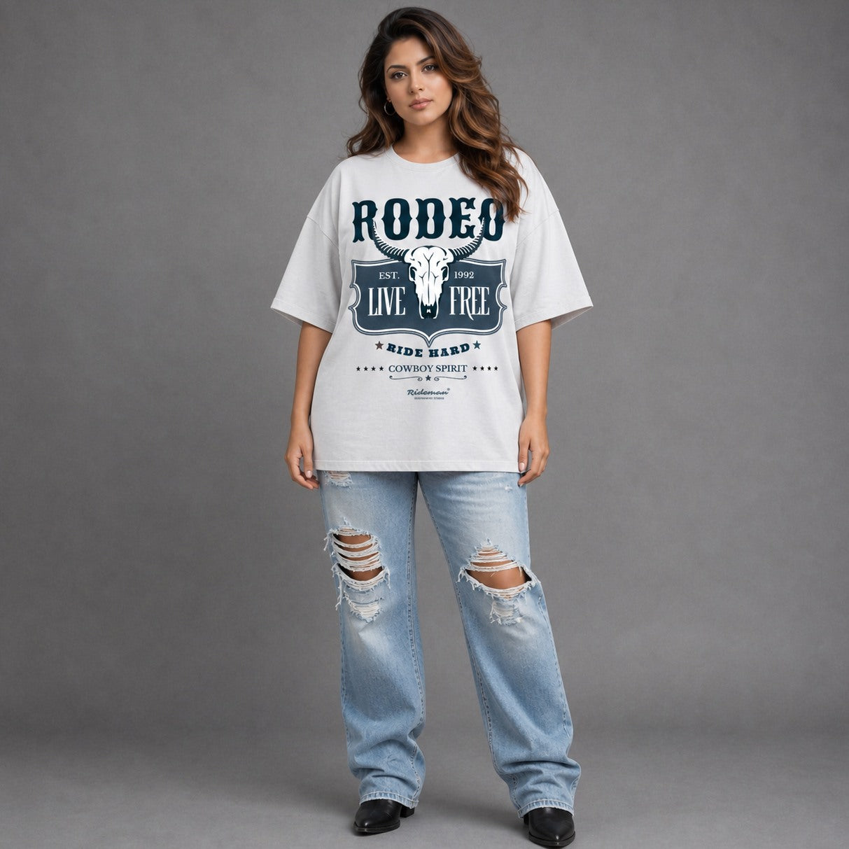 Woman wearing a white 'Rodeo' t-shirt and ripped jeans on a gray background
