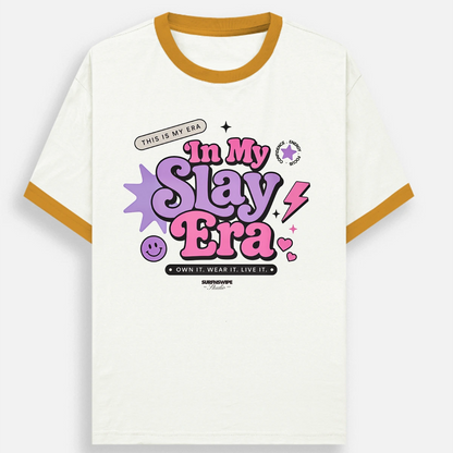 A ringer t-shirt with an off-white body, mustard yellow collar and sleeve trim, featuring a colorful graphic on the chest that reads 'In My Slay Era' in pink and purple bubble letters with a smiley face and lightning bolt details.